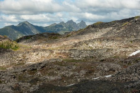 Zerklüftete Bergrücken erheben sich in der Ferne über sonnenbeschienene Felsen im Spray Park im Mount Rainier Nationalpark