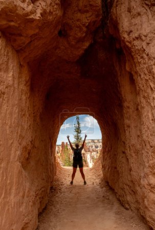 Mujer se para con los brazos arriba en el túnel de Hoodoo en Bryce Canyon
