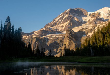 Faint Wisps Of Fog Hang Over Klapatche Lake Below A Glowing Mount Rainier at sunset