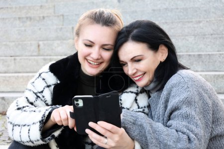 Foto de Dos mujeres sentadas afuera y mirando su teléfono - Imagen libre de derechos