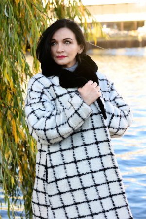 Photo for Beautiful woman in coat walking along a river in the city - Royalty Free Image