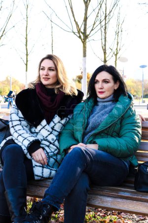 Téléchargez les photos : Portrait de deux femmes assises dehors sur un banc en manteaux - en image libre de droit