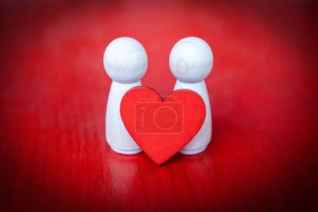 Photo for Two wooden figures holding a red heart on red background - Royalty Free Image