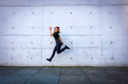 Photo for Young woman in black clothes jumping in front of grey wall - Royalty Free Image