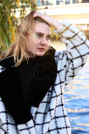 Photo for Young woman in a coat walking along a river in the city - Royalty Free Image