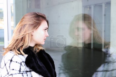 Photo for Young woman standing outside and looking at her reflection at window - Royalty Free Image