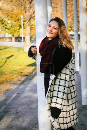 Téléchargez les photos : Jeune femme dans un manteau debout à l'extérieur dans le parc profiter du soleil - en image libre de droit