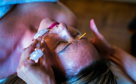Téléchargez les photos : Une femme subissant un traitement d'acupuncture sur le visage à l'aide d'un masseur facial Jade, un élément pour les procédures cosmétiques - en image libre de droit