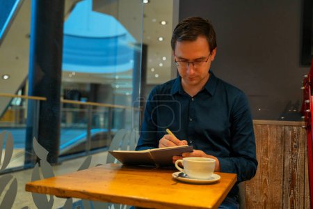 Photo for Thoughtful mature adult business man writing in notebook, middle aged author or writer taking notes thinking of new ideas, mature male student making checklist, learning in cafe sitting at table. - Royalty Free Image