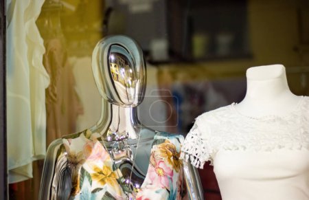 Téléchargez les photos : Mannequin chromé brillant mannequin debout dans une vitrine de magasin avec d'autres mannequins en arrière-plan - en image libre de droit