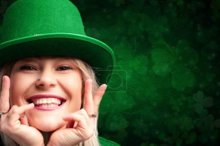 Lächelnde Frau in grünem Gewand mit Koboldmütze vor Kleeblattkulisse