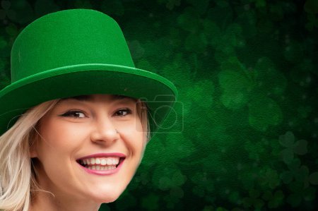 Lächelnde Frau in grünem Gewand mit Koboldmütze vor Kleeblattkulisse