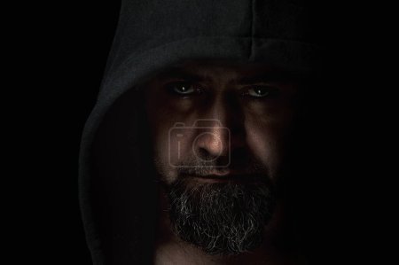 Photo for Close-up portrait of a man with a hood on a black background. Mysterious man wearing hoodies on a dark background. - Royalty Free Image