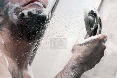 Photo for Man takes a shower. Shot of a young man taking a shower in the modern tiled bathroom. Lather it up. - Royalty Free Image