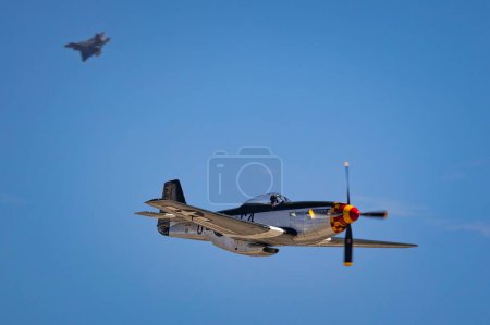 Foto de Un P-51 Mustang realiza un vuelo con un F-22 Raptor en el fondo en la Exposición Aérea Miramar 2022 en San Diego, California. - Imagen libre de derechos