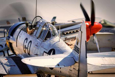 Foto de Un T-6 Texan espera un taxi mientras pasa un P-51 Mustang, ambos artistas en Warbirds Over Miramar en America 's Airshow 2023 en Miramar, California. - Imagen libre de derechos