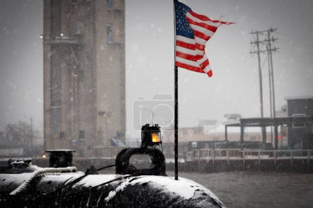Téléchargez les photos : Un drapeau américain sur la poupe de l'USS Cobia (SS245), lors d'une tempête de neige, et une partie du Wisconsin Maritime Museum à Manitowoc, Wisconsin. - en image libre de droit
