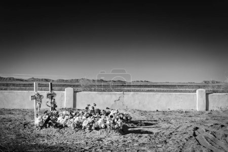 Téléchargez les photos : Tombes couvertes de fleurs au cimetière La Isla près de Fabens, Texas avec le mur frontalier américano-mexicain en arrière-plan. - en image libre de droit