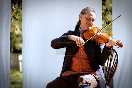 Photo for A violinist, in period clothing, performs a song in Colonial Williamsburg, Virginia. - Royalty Free Image