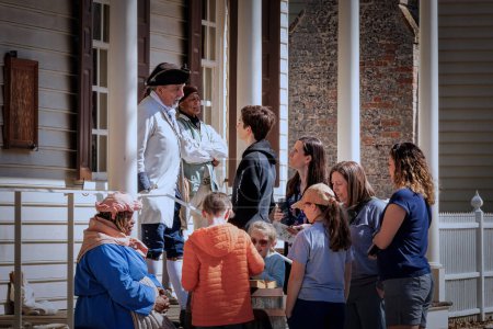 Photo for Tourists listen intently as a guide speaks at Colonial Williamsburg, Virginia. - Royalty Free Image