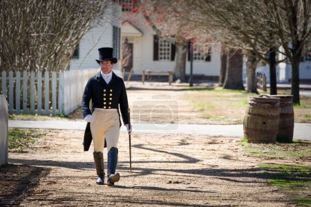 Photo for A man in a top hat walks on a walk-way, in period clothing, at Colonial Williamsburg, Virginia. - Royalty Free Image