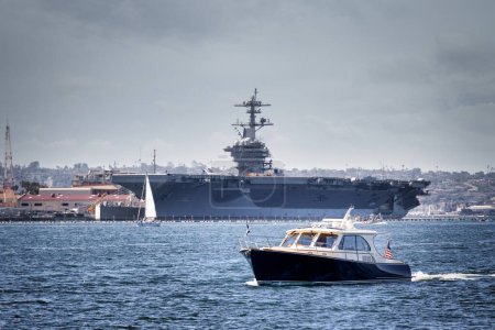 A boat on the water, with a US Navy aircraft carrier in background, at San Diego Bay off the coast of Coronado, California.