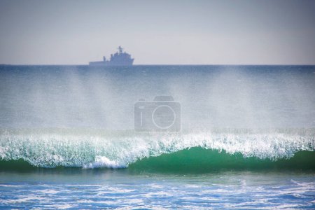 The Pacific Ocean surf rolls in, while a Navy ship sits on the distant horizon, at Coronado, California.