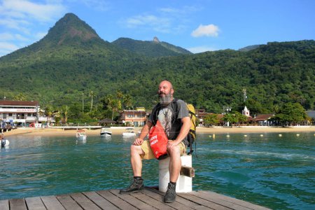 Téléchargez les photos : Homme avec barbe assis sur une jetée en bois dans l'océan. - en image libre de droit
