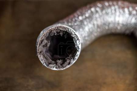Un conduit d'aération de séchoir en aluminium flexible sale rempli de peluches, de poussière et de saleté.