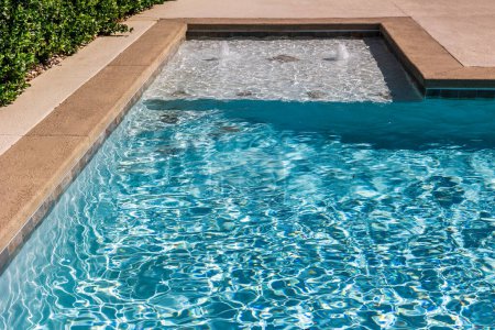 Téléchargez les photos : A rectangular new swimming pool with tan concrete edges in the fenced backyard of a new construction house. - en image libre de droit
