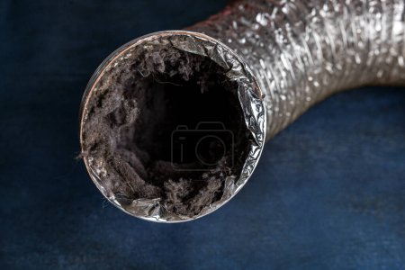 Un conduit de ventilation de séchoir en aluminium flexible sale de blanchisserie rempli de charpie, de poussière et de saleté sur un fond bleu.