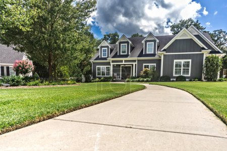 Photo for A large gray craftsman new construction house with a landscaped yard and leading pathway sidewalk on a sunny day with blue skies and clouds. - Royalty Free Image