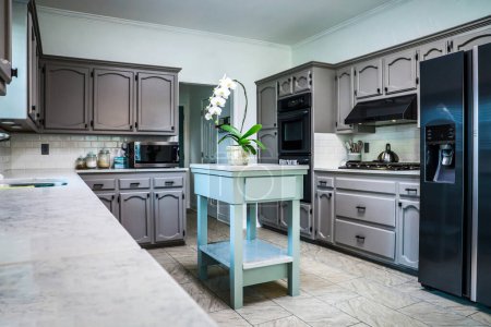 Photo for A renovated kitchen in an older home with painted gray cabinets, marble countertops, a small portable island and a tiled floor. - Royalty Free Image