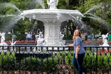eine alleinstehende Frau in ihren Vierzigern draußen in Savannah, Georgia im Frühling im Forsuth Park am Brunnen stehend mit Touristen im Hintergrund