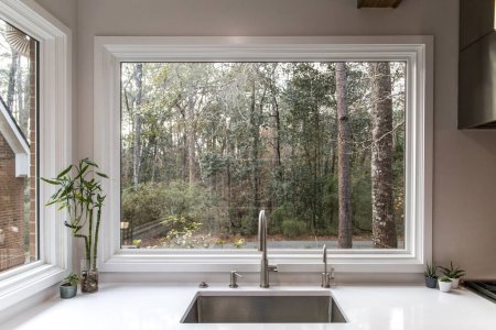 A large farmhouse single farm house sink with a massive picture window with a view of the wooded lot yard.
