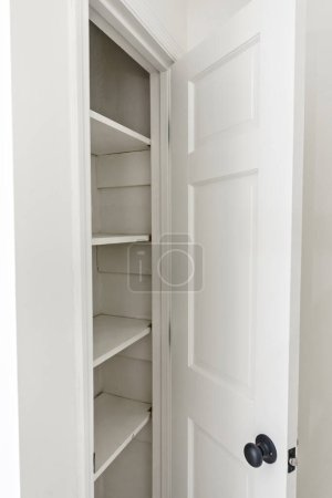 Interior white solid wood closet or kitchen pantry with wood shelves in an older house that has been newly renovated and painted with open door.