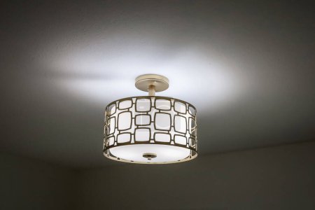 Photo for An elegant gold and white electric lighting fixture illuminating a dark bedroom. - Royalty Free Image
