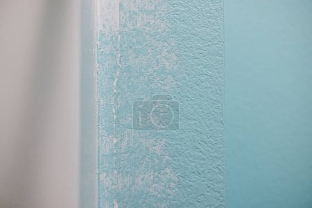 Crack in a bathroom wall between the textured blue aqua wall and shower bathtub insert that has been filled and evened and is ready to be painted