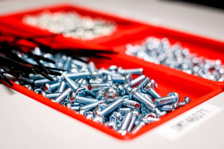 Foto de Montones de tornillos en una caja roja, fábrica, fabricación electrónica. Desenfocado. Foto de alta calidad - Imagen libre de derechos