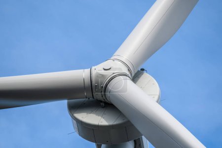 Closeup of the hub of a large wind turbine, looking up at an angle. Blue sky behind.