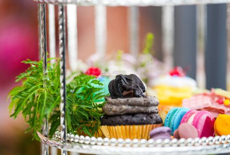 Téléchargez les photos : Après-midi thé ou High Tea Display dans le rack d'argent avec des fleurs, macaron, scone, gâteau, gâteaux de tasse, sur fond coloré - en image libre de droit