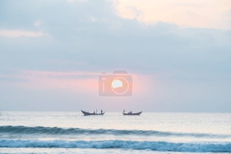 Foto de Paisaje de pequeñas embarcaciones pesqueras de pescadores vietnamitas que pescan al amanecer en el mar, con sol naciente, nubes y cielo. Paisaje marino al amanecer y atardecer en hermoso amarillo y naranja. - Imagen libre de derechos