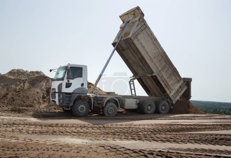 Foto de Camión volquete gris en el sitio de construcción en el proceso de transporte de descarga de suelo. Excavación. Vehículo comercial para la construcción - Imagen libre de derechos