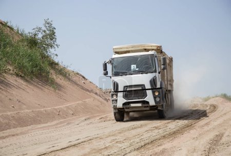 Téléchargez les photos : Camion à benne grise balade sur un chemin de terre dans le processus de transport. Véhicule utilitaire pour les entreprises de construction en travaux - en image libre de droit