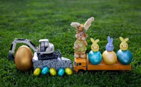 greeting card for business congratulations of construction companies on Easter holiday. Composition of a model of an excavator, dump trucks, painted eggs, Easter bunnies standing on the grass.