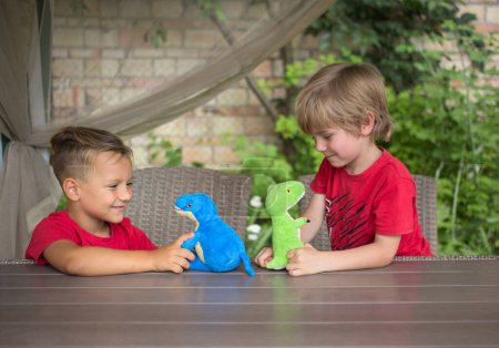 Foto de Two boys play at table with plush dinosaurs in role-playing games. Communication with friends, joy, positive. Fun activity for friends. Interesting childhood. Selective focus. Brothers connection - Imagen libre de derechos