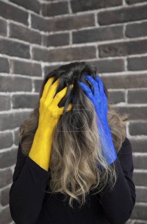 Photo for Unrecognizable woman with hair covering her face in desperation holds head in hands, painted in colors of Ukrainian flag. suffering of civilians. Stop war. Fear and powerlessness. Stay with Ukraine - Royalty Free Image