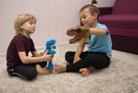 Foto de Preschool boys play role playing games with dinosaur toys while sitting on rug. Communication with friends, friendship between brothers, entertainment for children, joyful childhood. selective focus. - Imagen libre de derechos