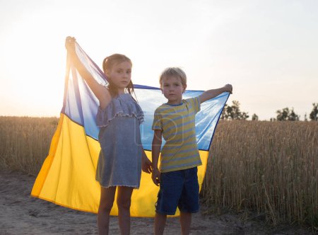 Photo for Children stand in a wheat field with a blue and yellow Ukrainian flag in the backlight of the setting sun. unity, support, patriotism. Ukrainians are against the war. Pride, freedom, national symbol - Royalty Free Image
