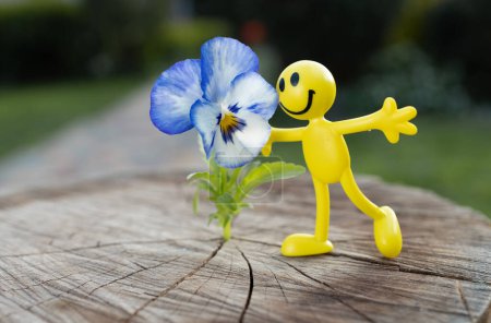 Foto de Figura de juguete brillante en miniatura de una pequeña gente alegre y amarilla cerca de una flor afeminado. concepto de amor, alegría, felicidad. pensamiento positivo. Regalo floral. feliz infancia - Imagen libre de derechos